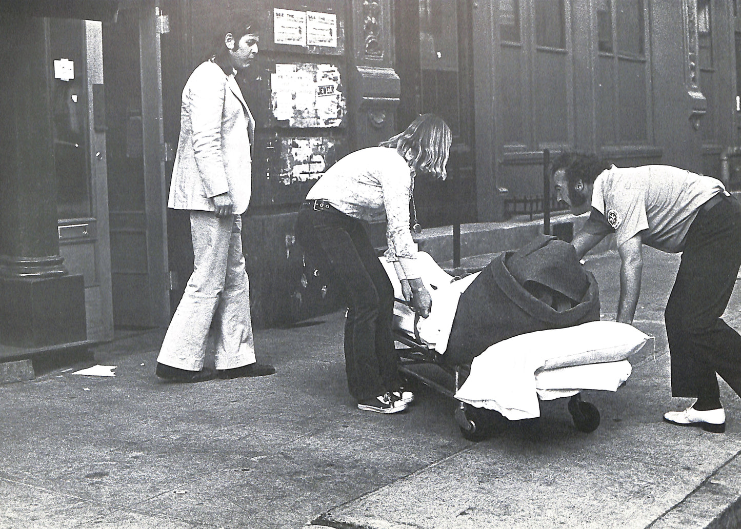 Interior page - CAROLINE TISDALL / JOSEPH BEUYS: COYOTE. Black and white photo of a person being pushed in a wheelchair by two others on a city street.
