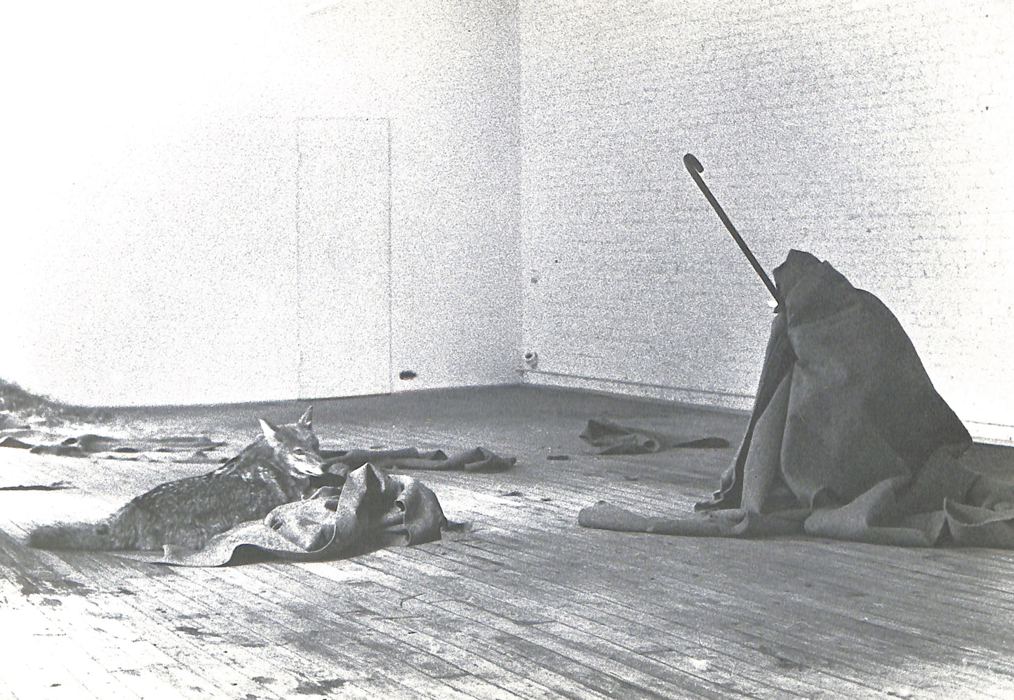 Black and white photograph of a person sitting on the floor with a stick in a minimalistic room.