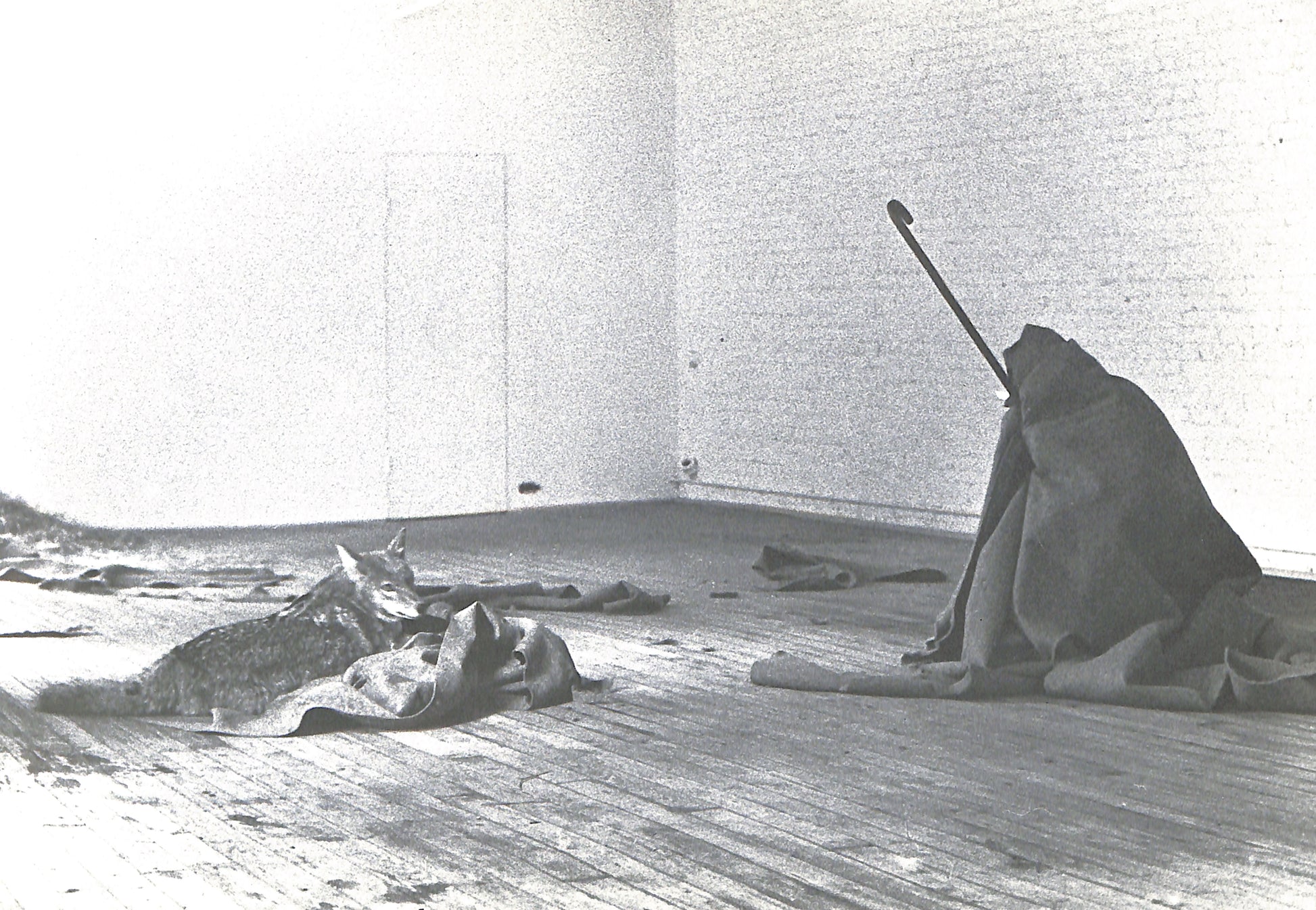 Black and white photograph of a person sitting on the floor with a stick in a minimalistic room.